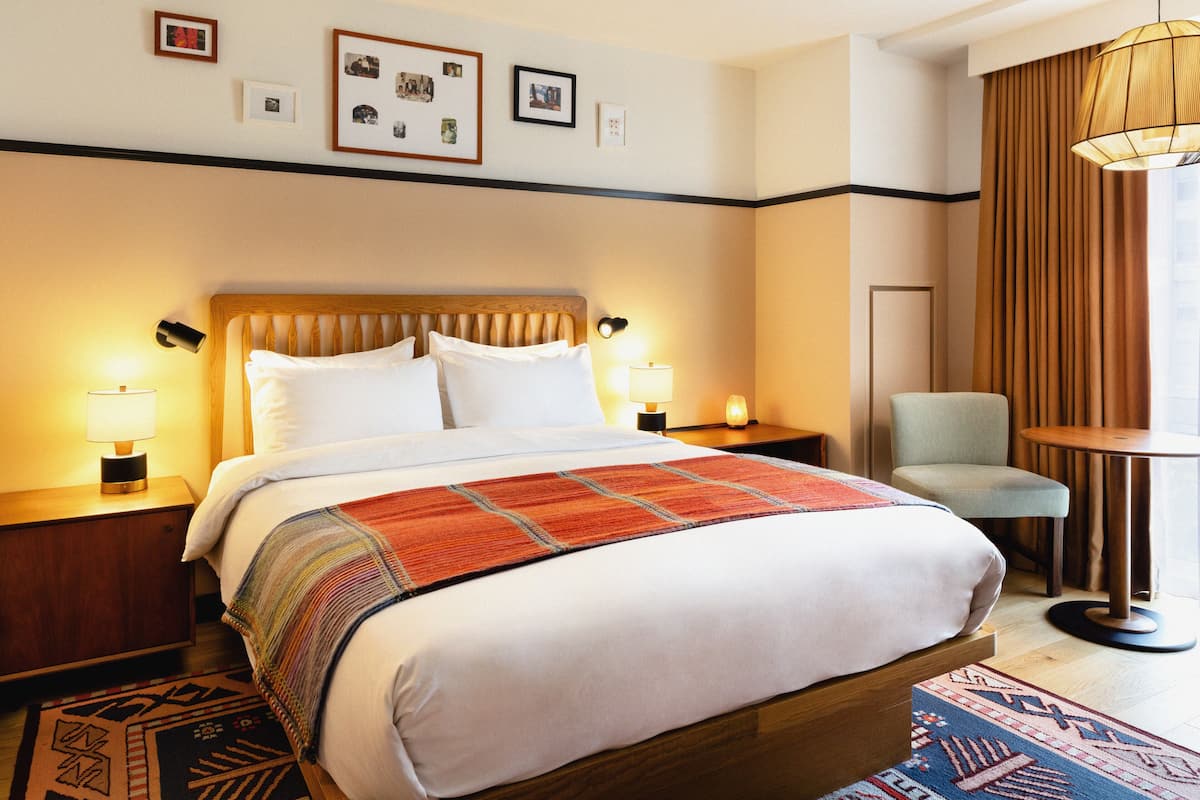 A hotel room with a large bed, two bedside tables with lamps, a chair, a small table, and a patterned rug.