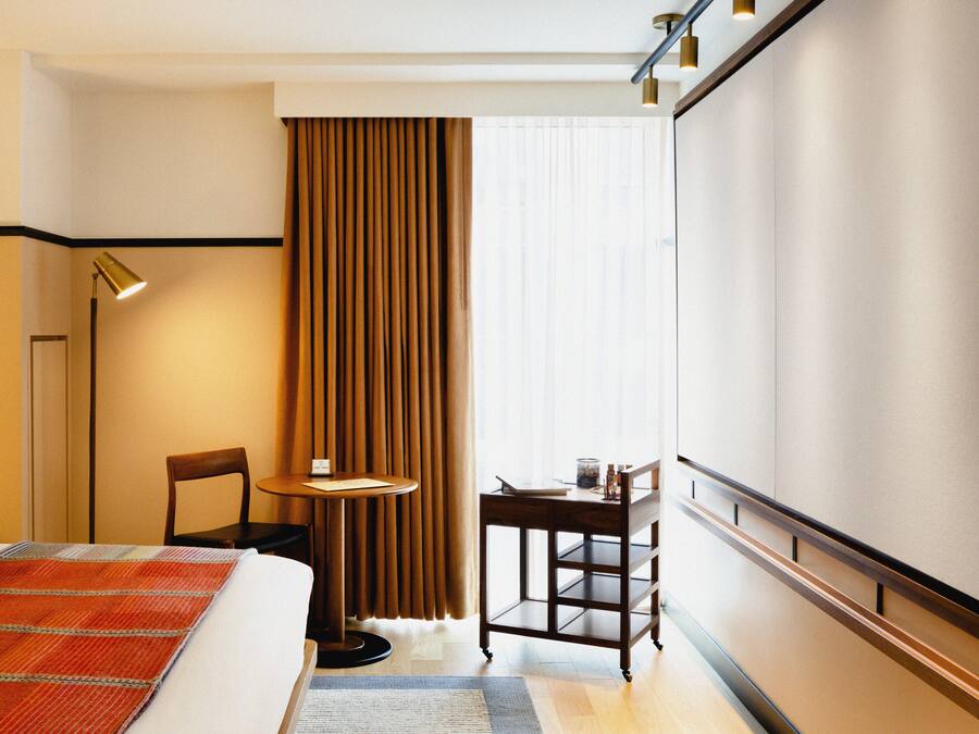 Habitación de hotel con cama, escritorio, silla, lámpara y ventana con cortinas.