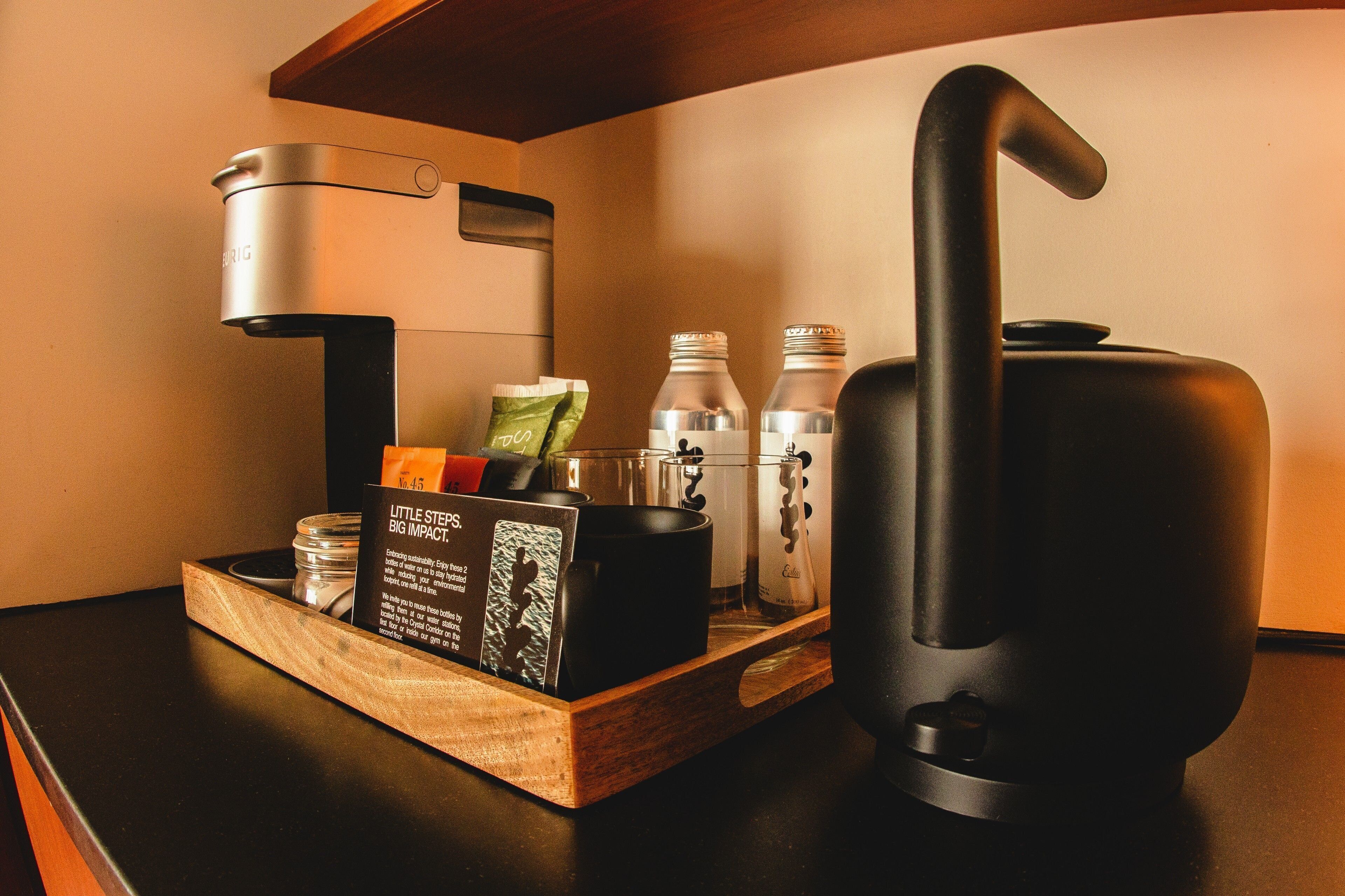 Een koffieapparaat, een waterkoker en een dienblad met een koffiekapsel, een mok en een glas water op een houten dienblad.