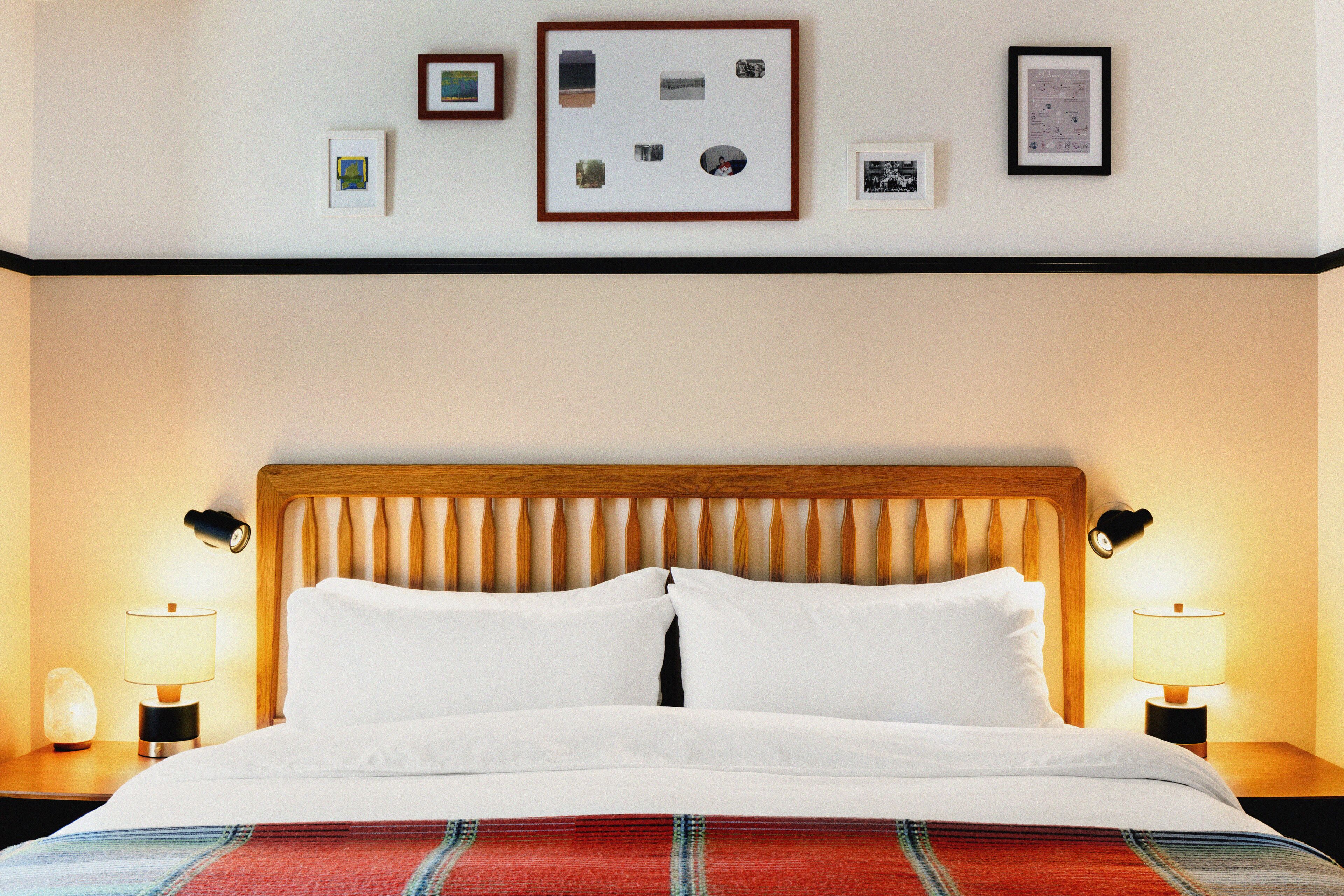 Una habitación de hotel con cabecera de madera, ropa de cama blanca y un collage enmarcado en la pared.