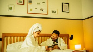 A hotel room with a bed, a nightstand, and a wall with framed pictures.