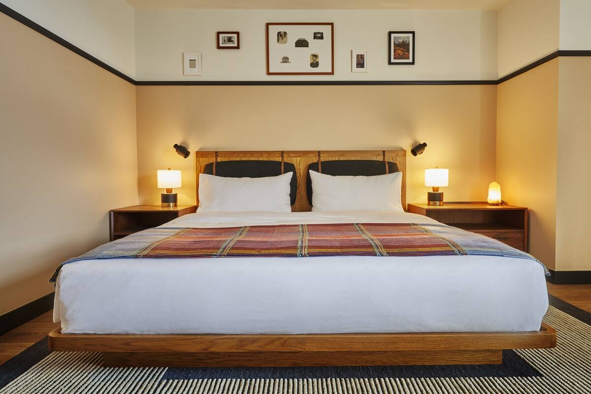 A neatly made bed with a colorful blanket, two bedside tables with lamps, and framed pictures on the wall.
