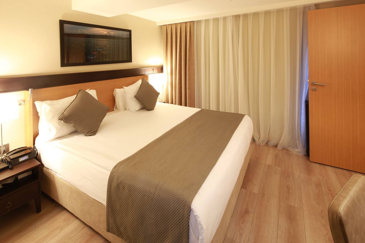 A hotel room with a large bed, a wooden headboard, a nightstand with a telephone, and a door to the right.