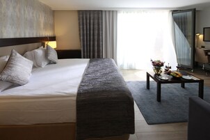 A hotel room with a large bed, a bedside table with a vase of flowers, and a dining table set for two.