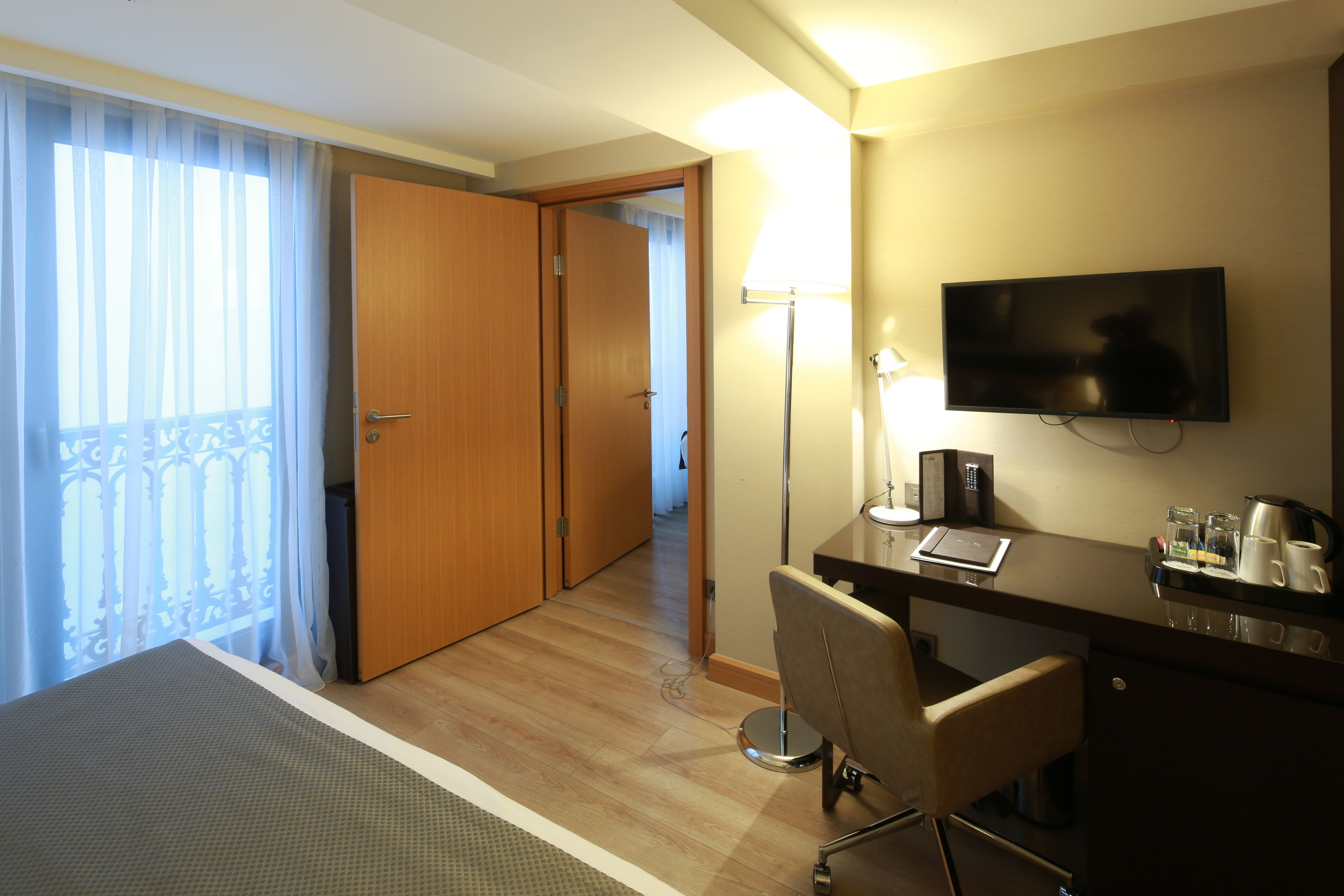 Habitación de hotel con cama, escritorio con silla, televisión, lámpara y cafetera.