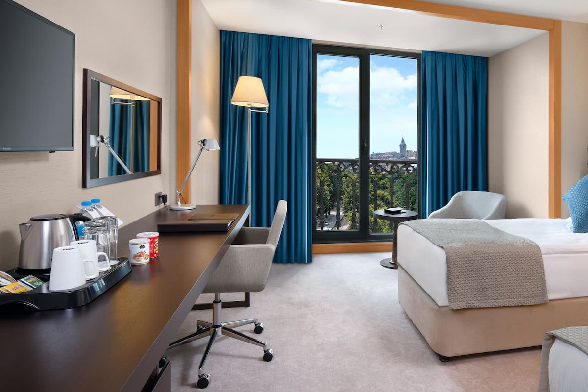 A hotel room with a bed, desk, chair, and a large window with curtains.