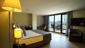 Habitación de hotel con cama, escritorio, silla, televisor y balcón con vistas a la ciudad.