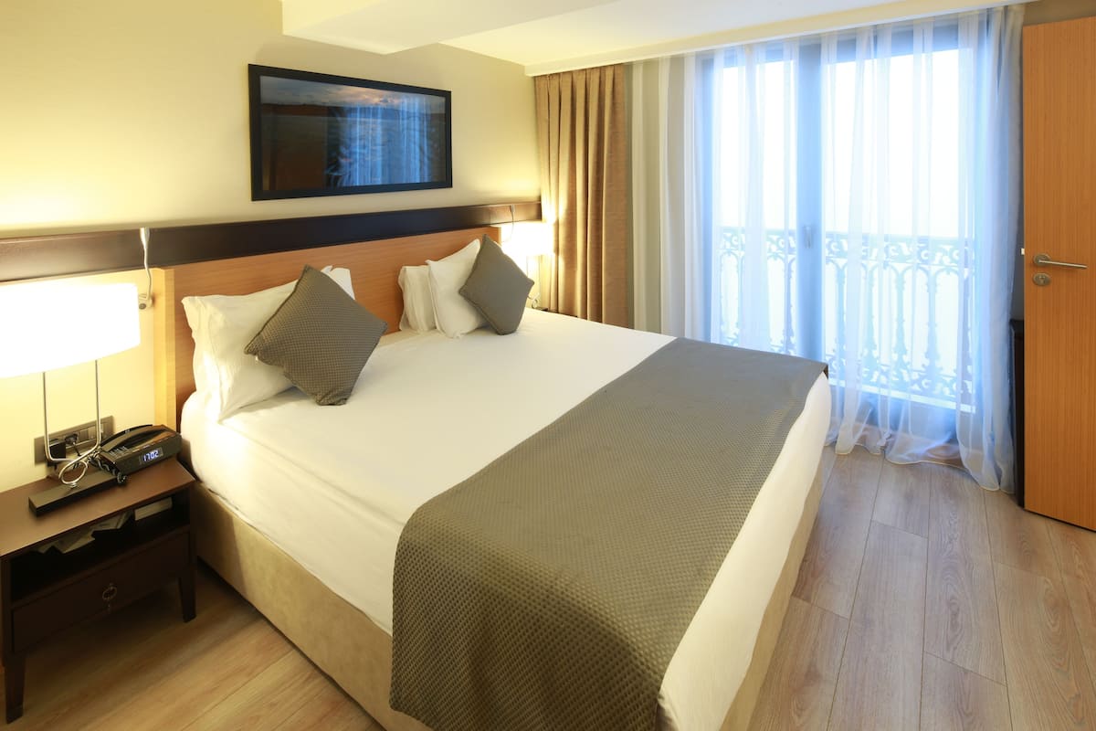 A hotel room with a large bed, a bedside table with a phone, a TV mounted above the bed, and a window with curtains.