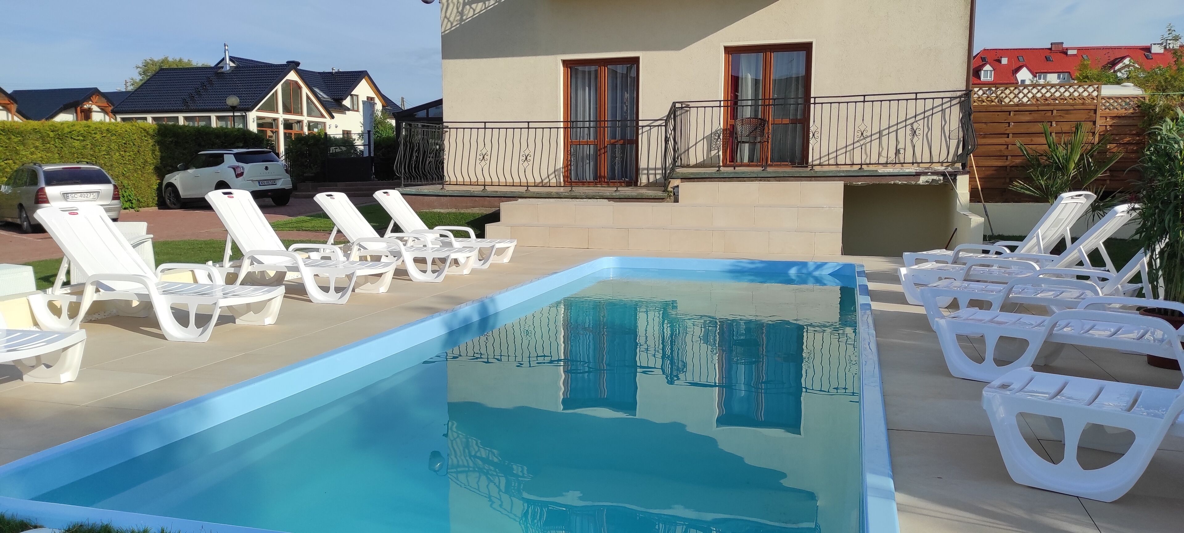 Une piscine entourée de chaises longues blanches, avec un bâtiment doté d’un balcon en arrière-plan.