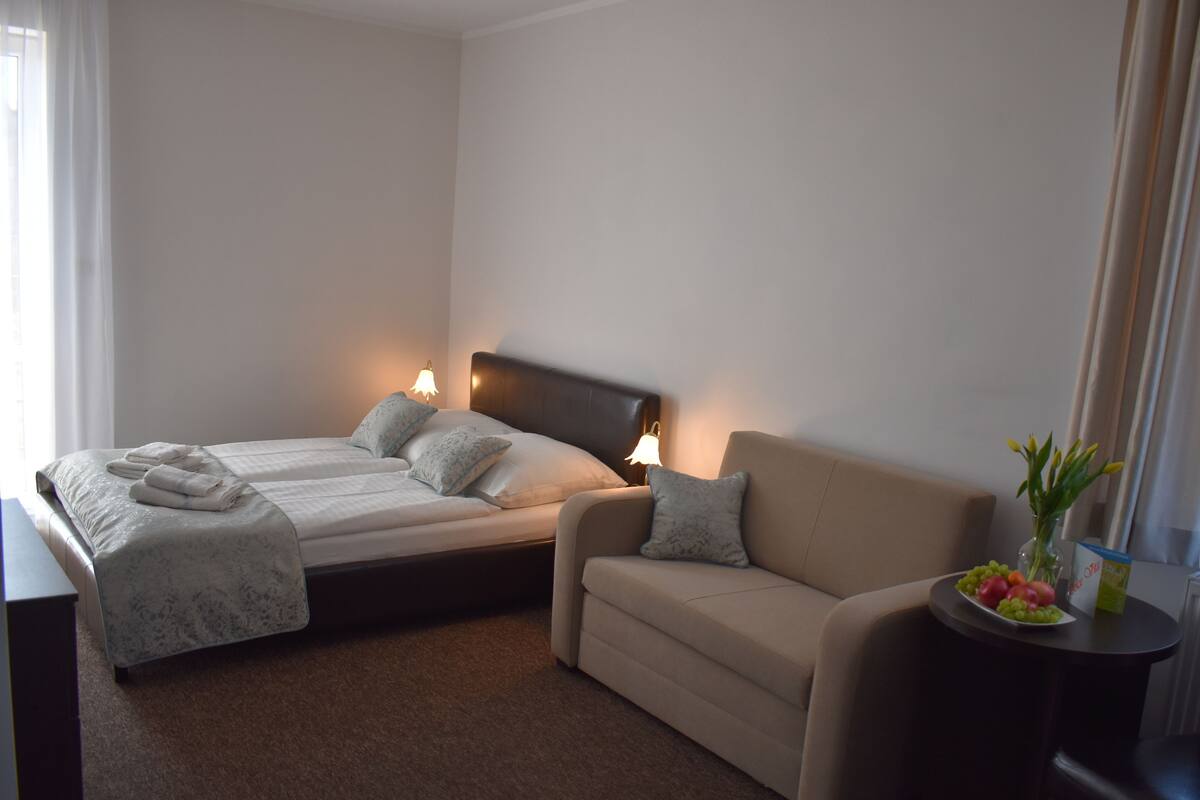 A hotel room with a bed, a sofa, and a small table with fruit.