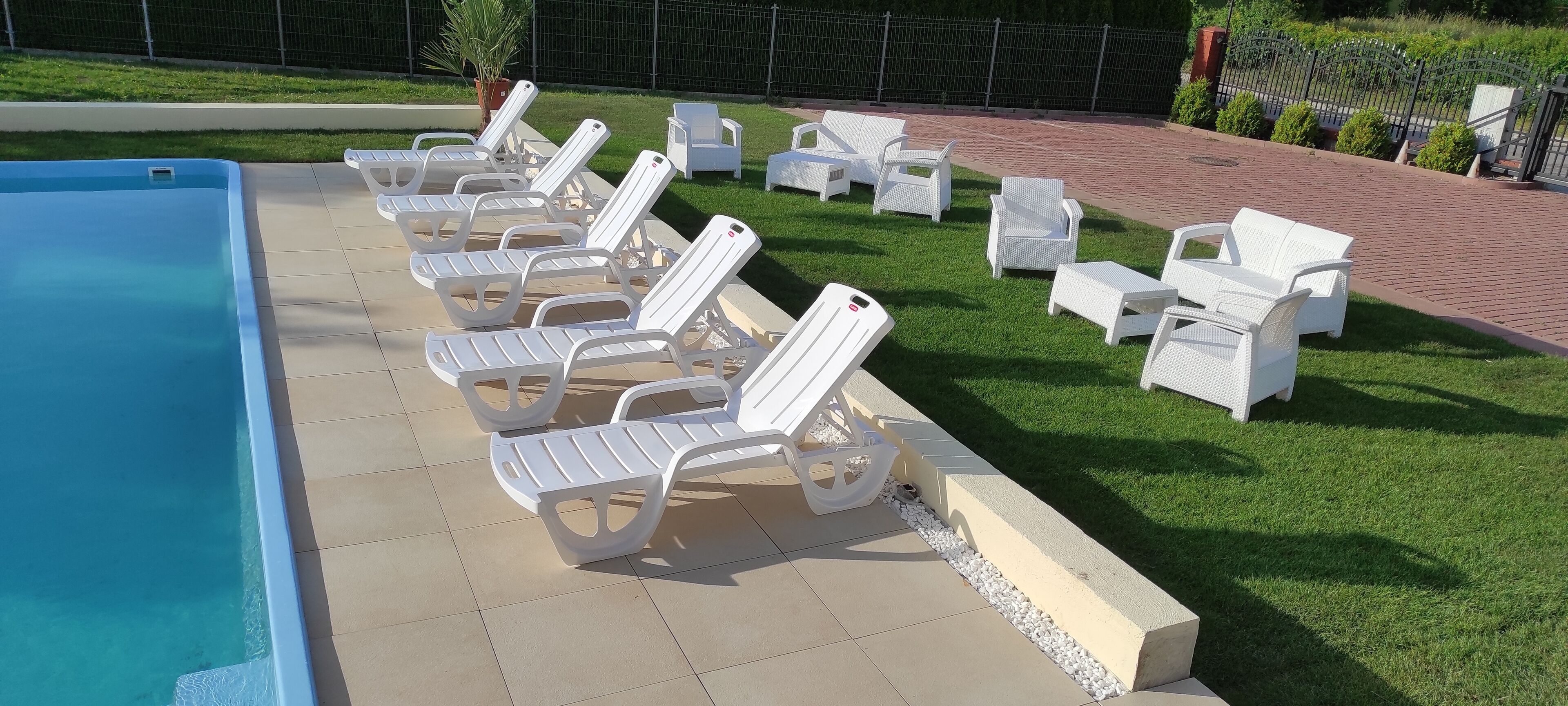 Ein Poolbereich mit weißen Liegestühlen und einer gefliesten Terrasse.