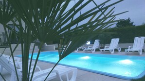 A swimming pool with white lounge chairs and a palm tree in the foreground. - Dolce  Vita (Ustronie Morskie)