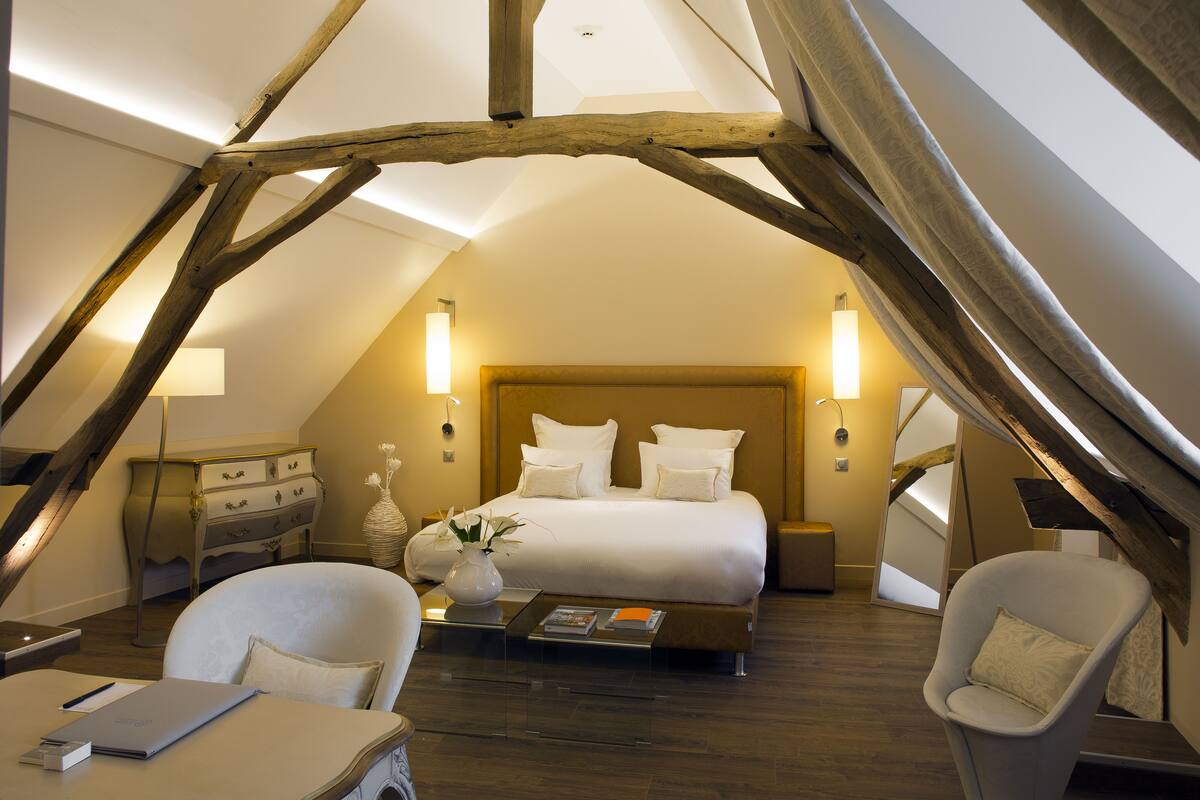 A bedroom with a sloped ceiling, a bed, two chairs, a bedside table, and a nightstand.