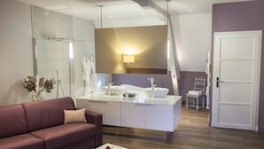 Un baño moderno con cabina de ducha de vidrio, un tocador blanco con un espejo grande y piso de madera.