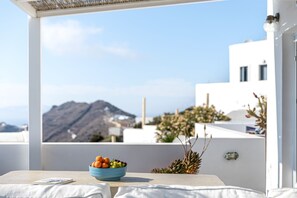 A table with a bowl of fruit and a book on a balcony with a mountain view. - The Nook (Santorini)