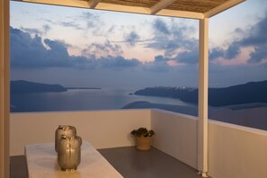 A balcony with a view of the sea and distant hills, a potted plant, and two metallic vases. - The Nook (Santorini)