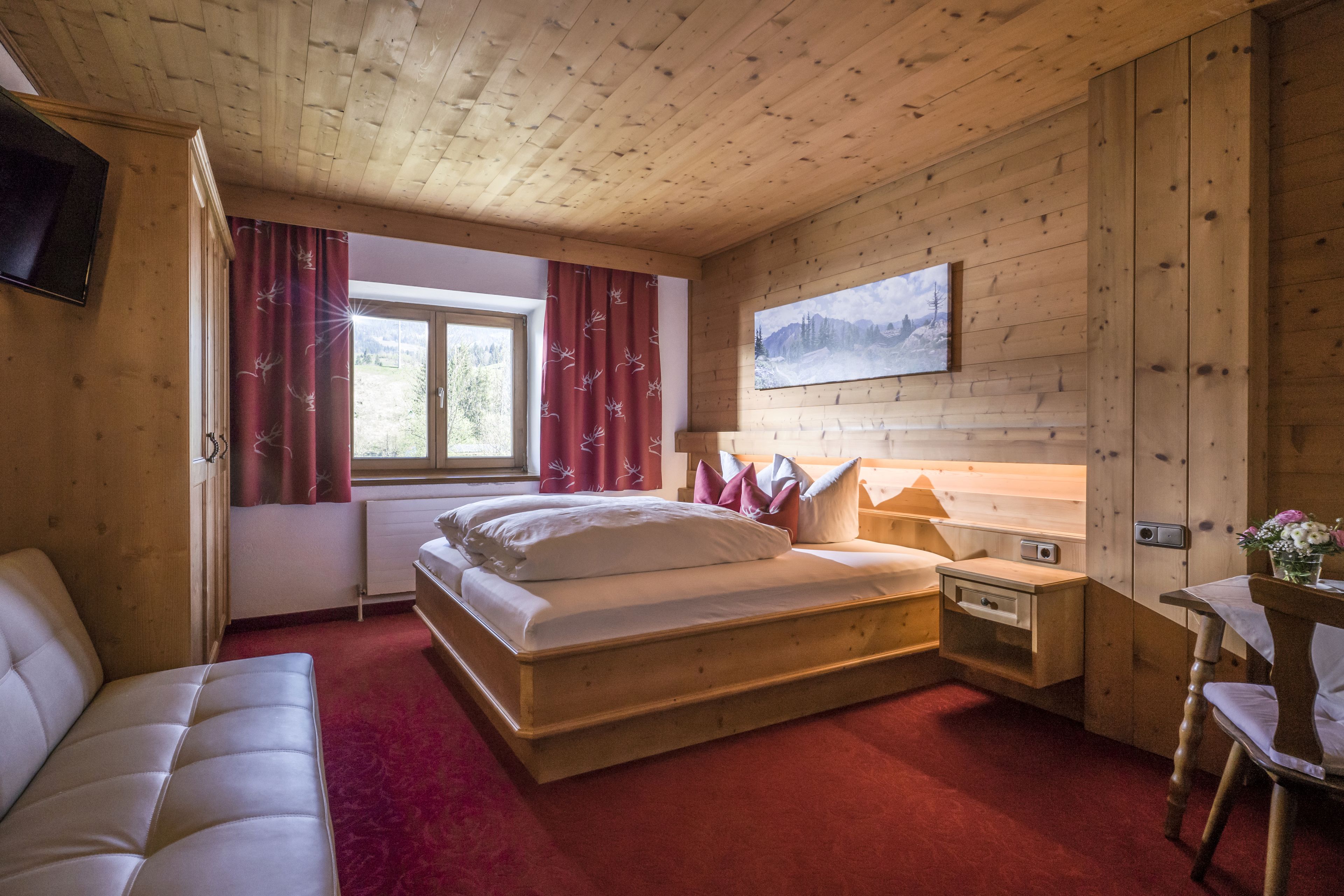 A wooden cabin bedroom with a bed, a nightstand, a chair, a table, and a painting on the wall.