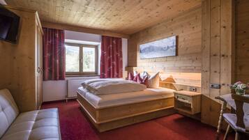 A wooden cabin bedroom with a bed, a nightstand, a chair, a table, and a painting on the wall.
