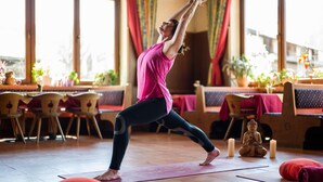A yoga class in a room with a wooden floor, yoga mats, and a statue of Buddha. - Pension Hüttwirt (Koessen)