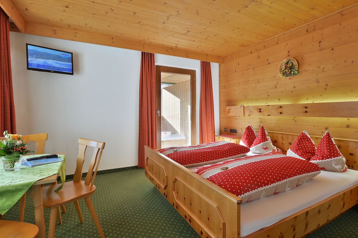 Una habitación de madera con una cama, una mesa, sillas y un televisor en la pared.