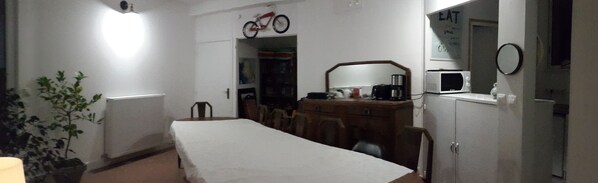 Una habitación pequeña y con poca luz, con una cama individual, un escritorio, una silla, un radiador, un microondas y un refrigerador.