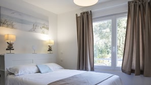 Una cama bien hecha con sábanas blancas, un plaid beige y dos lámparas de noche con pantallas.