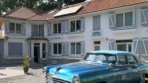 Un coche clásico color turquesa estacionado frente a un edificio blanco con varias ventanas y contraventanas.