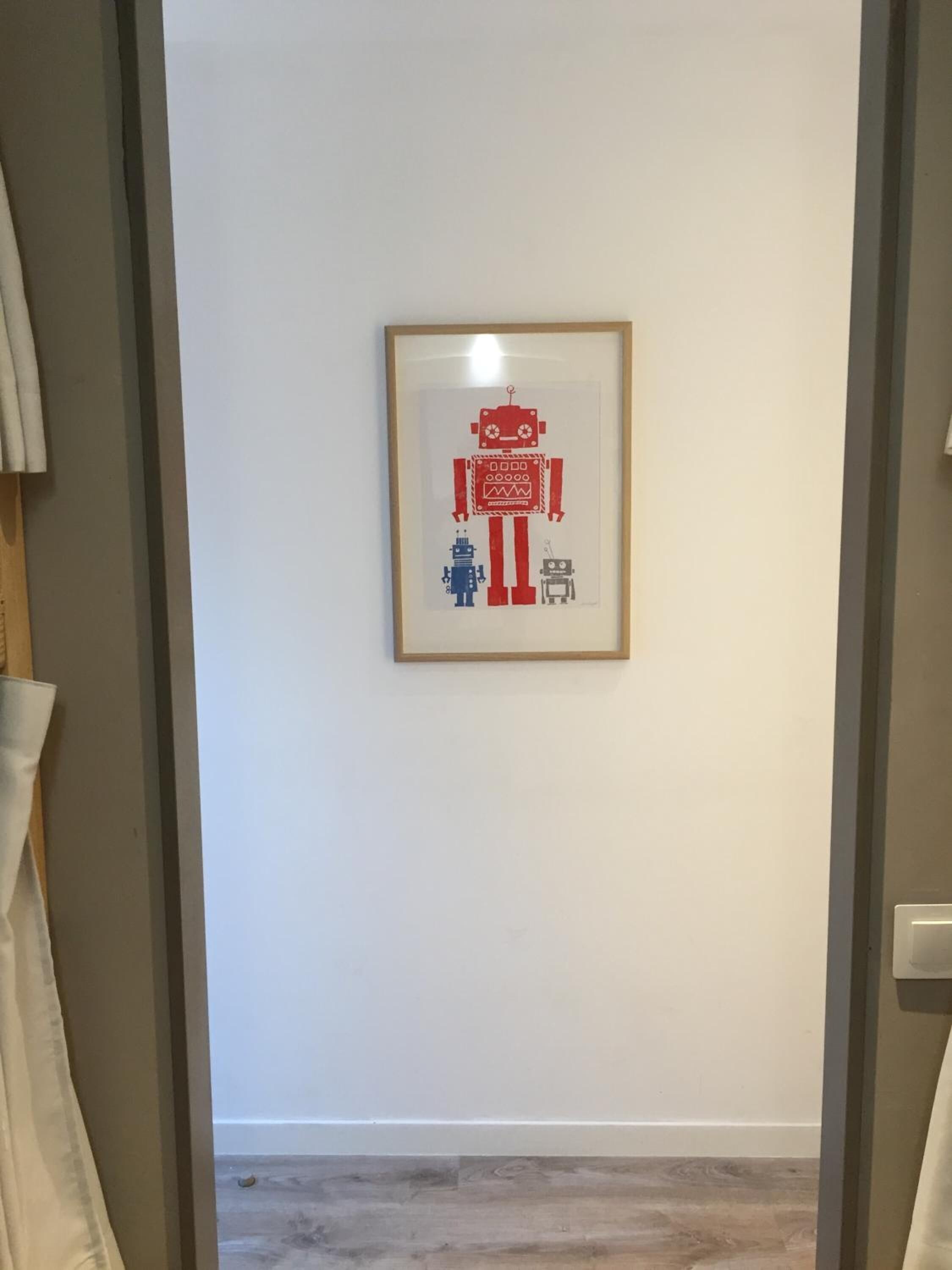 A framed artwork of a robot on a white wall in a hallway.