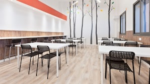 A modern conference room with white tables and black chairs, a wooden accent wall, and a tree decal on the wall. - ANT Hostel Barcelona (Barcelona)
