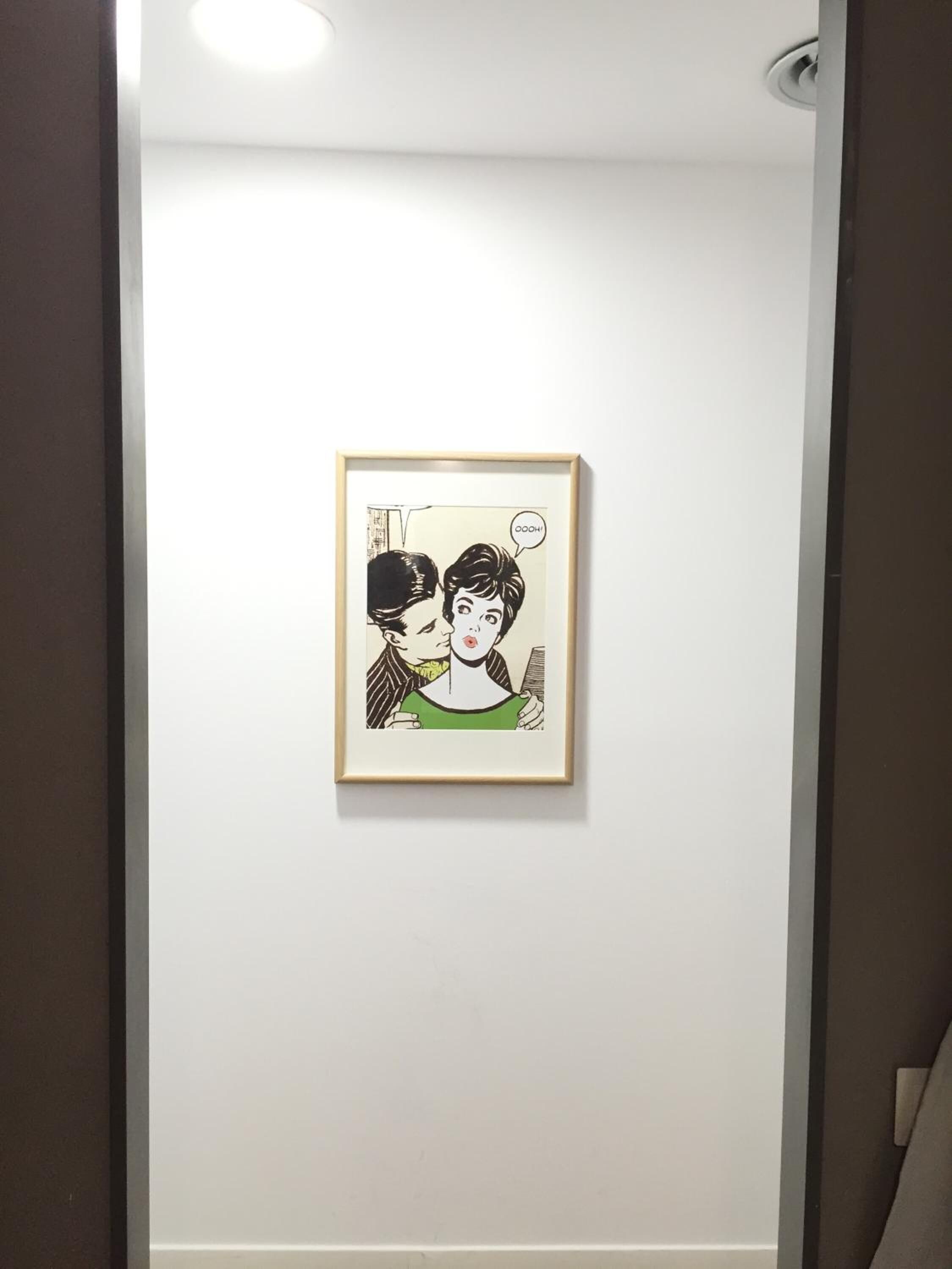 A framed artwork on a white wall in a hallway.
