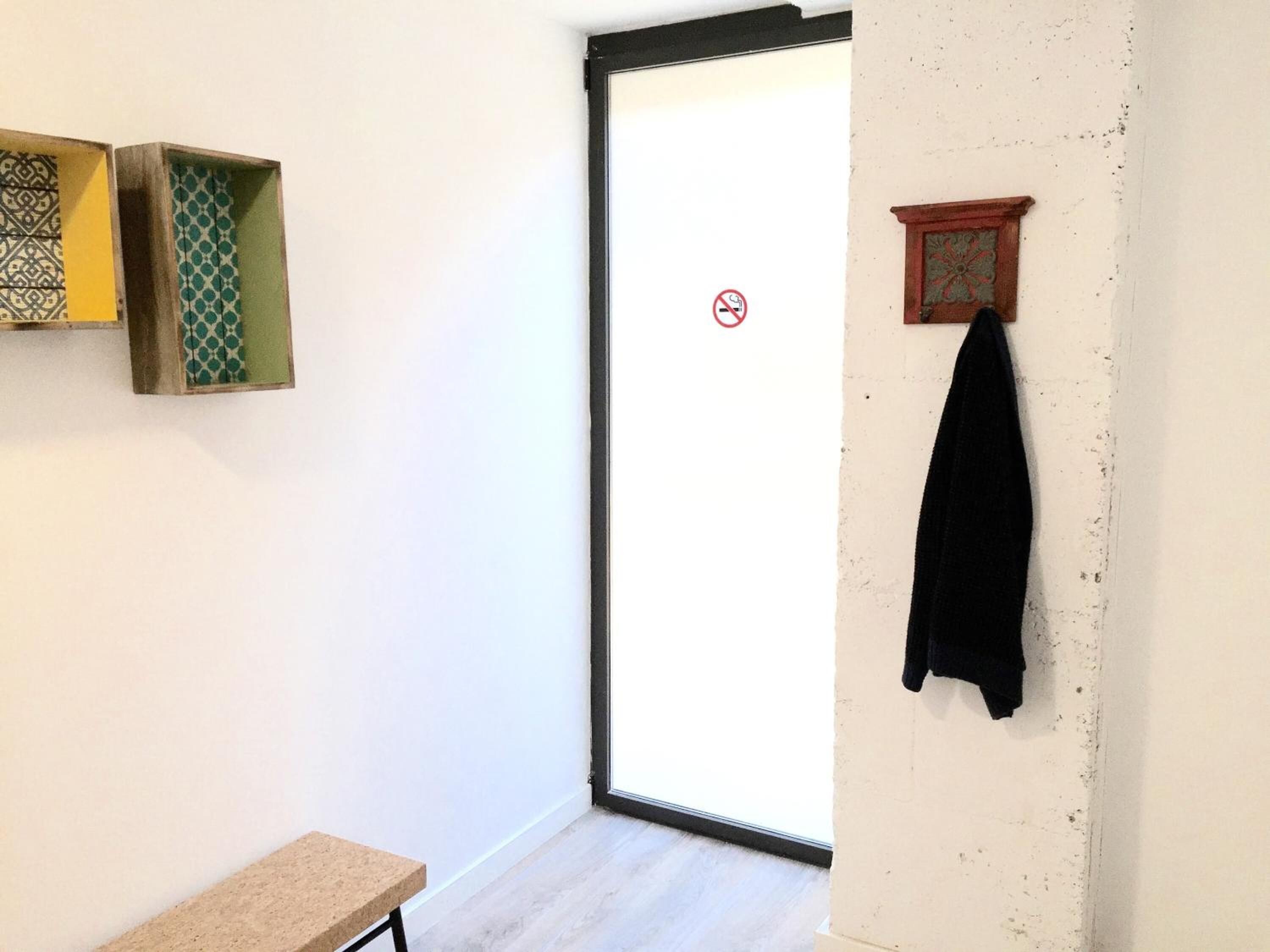Quarto com porta de correr de vidro, um banco e um cabideiro com uma peça de roupa preta.