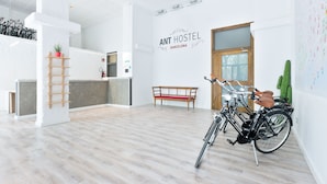A spacious room with a wooden floor, a bench, a bicycle, and a wall-mounted sign reading "ANT HOSTEL BARCELONA". - ANT Hostel Barcelona (Barcelona)