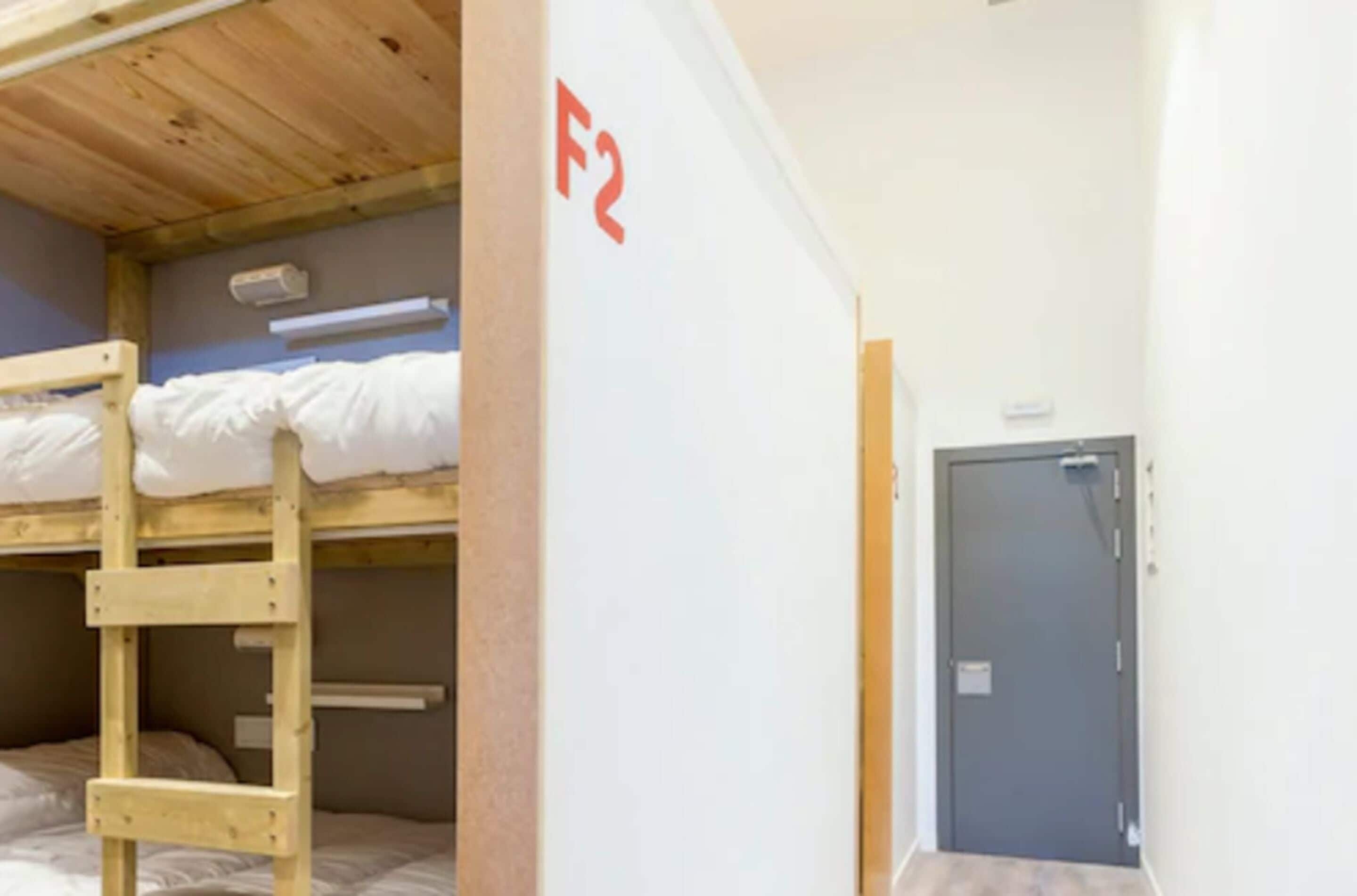 Quarto com beliche, escada de madeira, parede branca com um sinal vermelho 'F2' e uma porta.