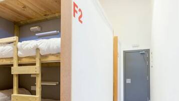 Quarto com beliche, escada de madeira, parede branca com um sinal vermelho 'F2' e uma porta.