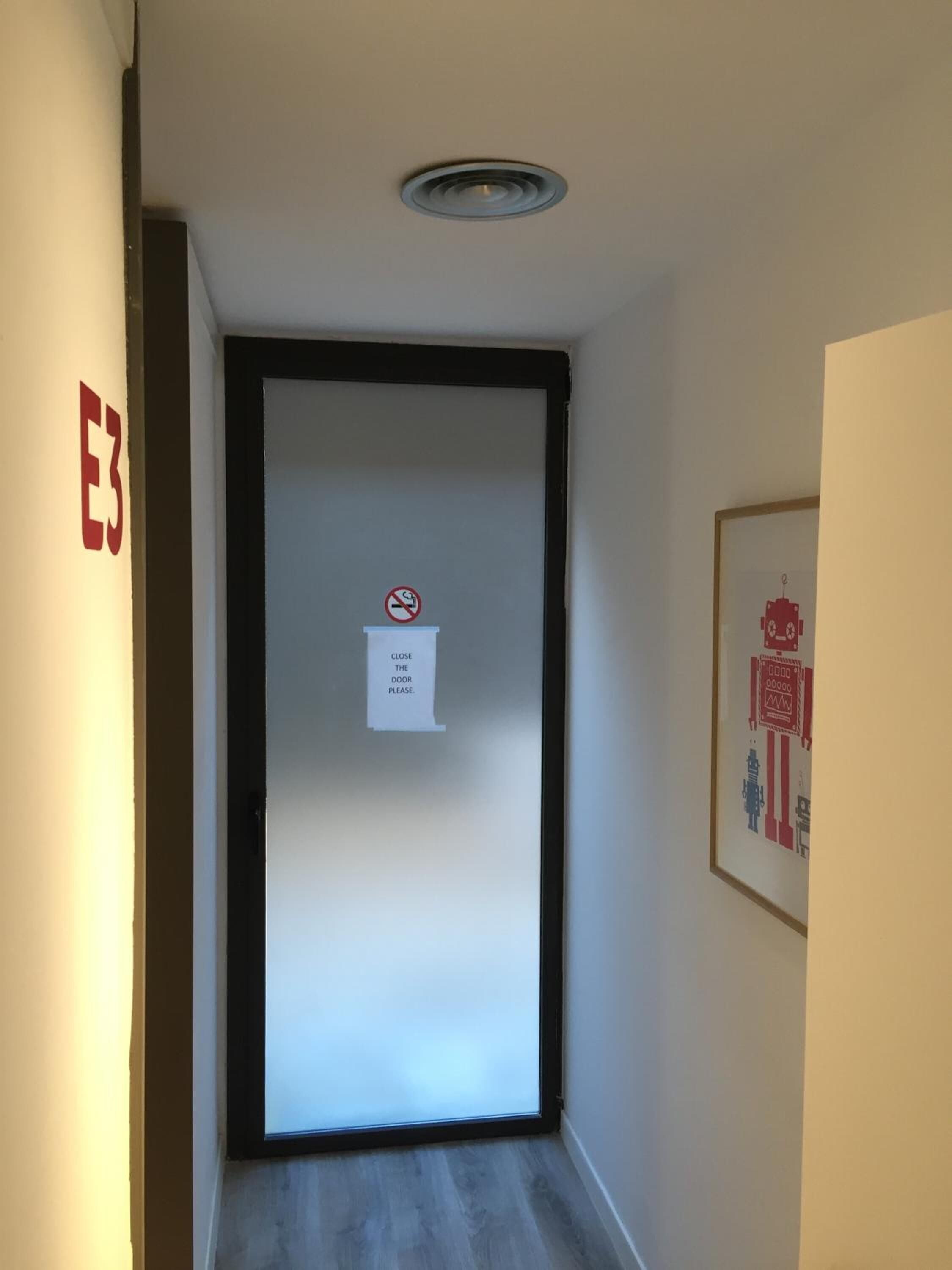 Un pasillo estrecho con una puerta marcada 'E3' y un cartel de 'No fumar'.