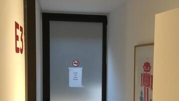 Un pasillo estrecho con una puerta marcada 'E3' y un cartel de 'No fumar'.