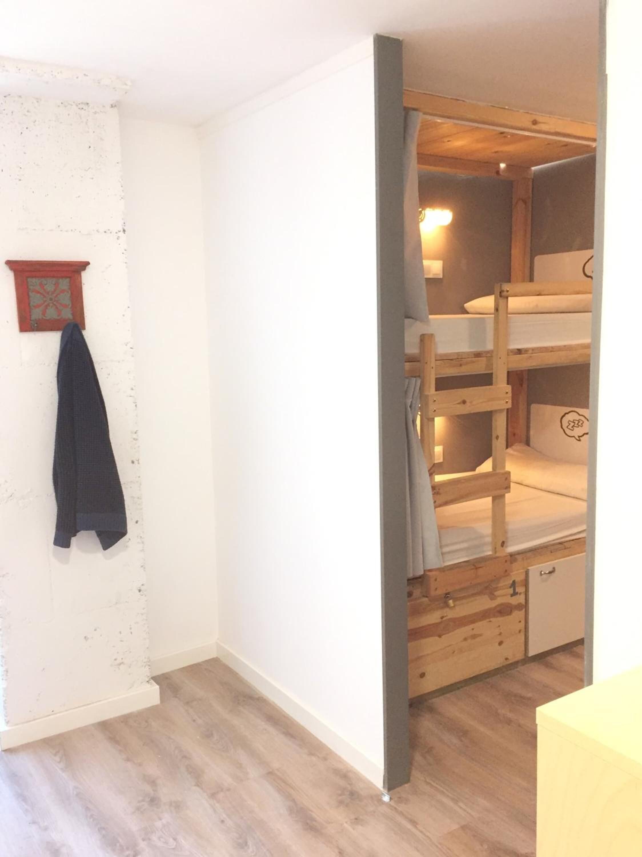 Una habitación con una cama litera, un armario pequeño y una lámpara fijada a la pared.