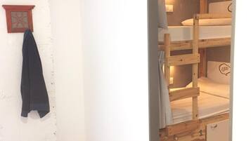 Una habitación con una cama litera, un armario pequeño y una lámpara fijada a la pared.