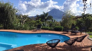A swimming pool with a brick deck, surrounded by lounge chairs and greenery, with a mountain in the background. - Casa Hagan (Santa Cruz La Laguna)