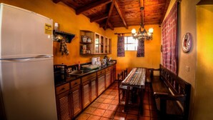 A compact kitchen with a refrigerator, wooden cabinets, a dining table, and a chandelier. - Casa Hagan (Santa Cruz La Laguna)