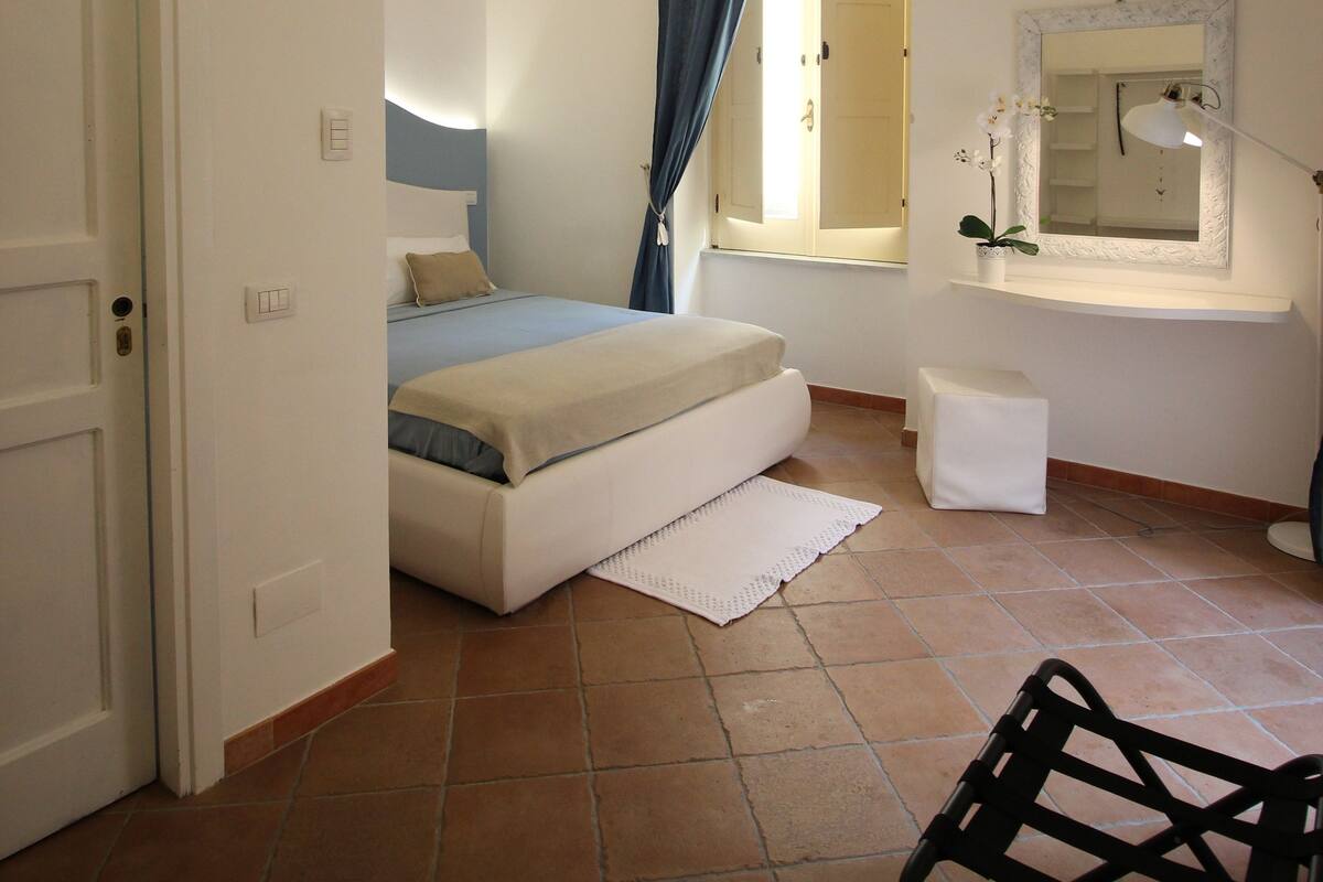 A bedroom with a bed, a bedside table, a mirror, and a chair.