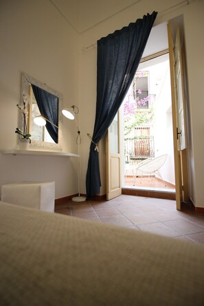Ein Badezimmer mit einer weißen Badewanne, einem Spiegel, einer Stehlampe und Blick auf einen Außenbalkon mit einem Stuhl.