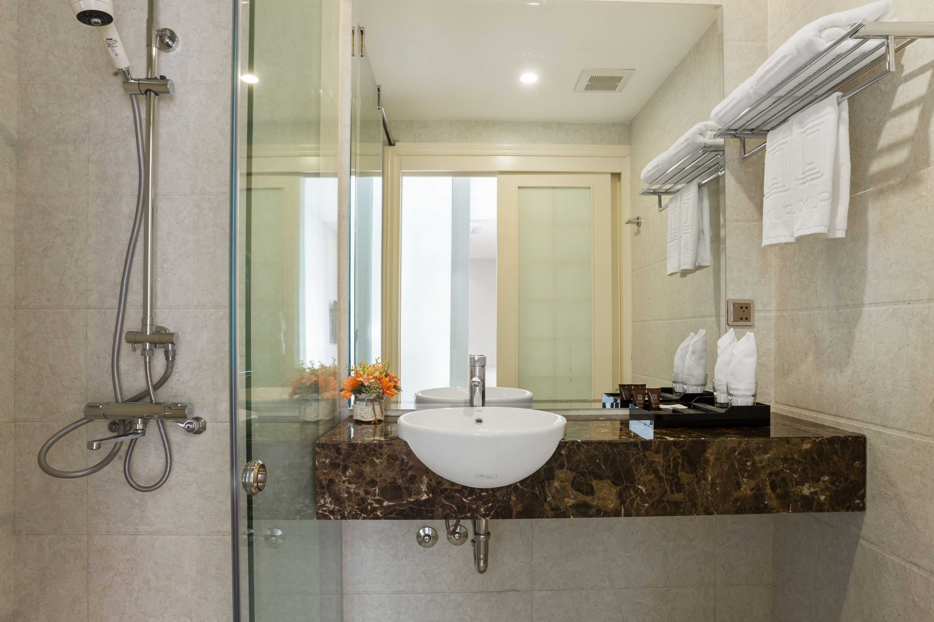A modern bathroom with a glass shower enclosure, a marble countertop, a white sink, and a mirror with a towel rack.