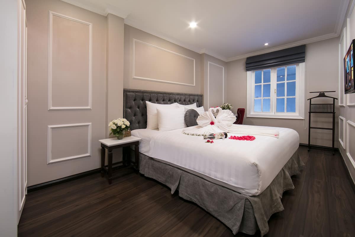 Een netjes ingerichte slaapkamer met een groot bed, een nachtkastje met een bloevas en een raam met uitzicht.