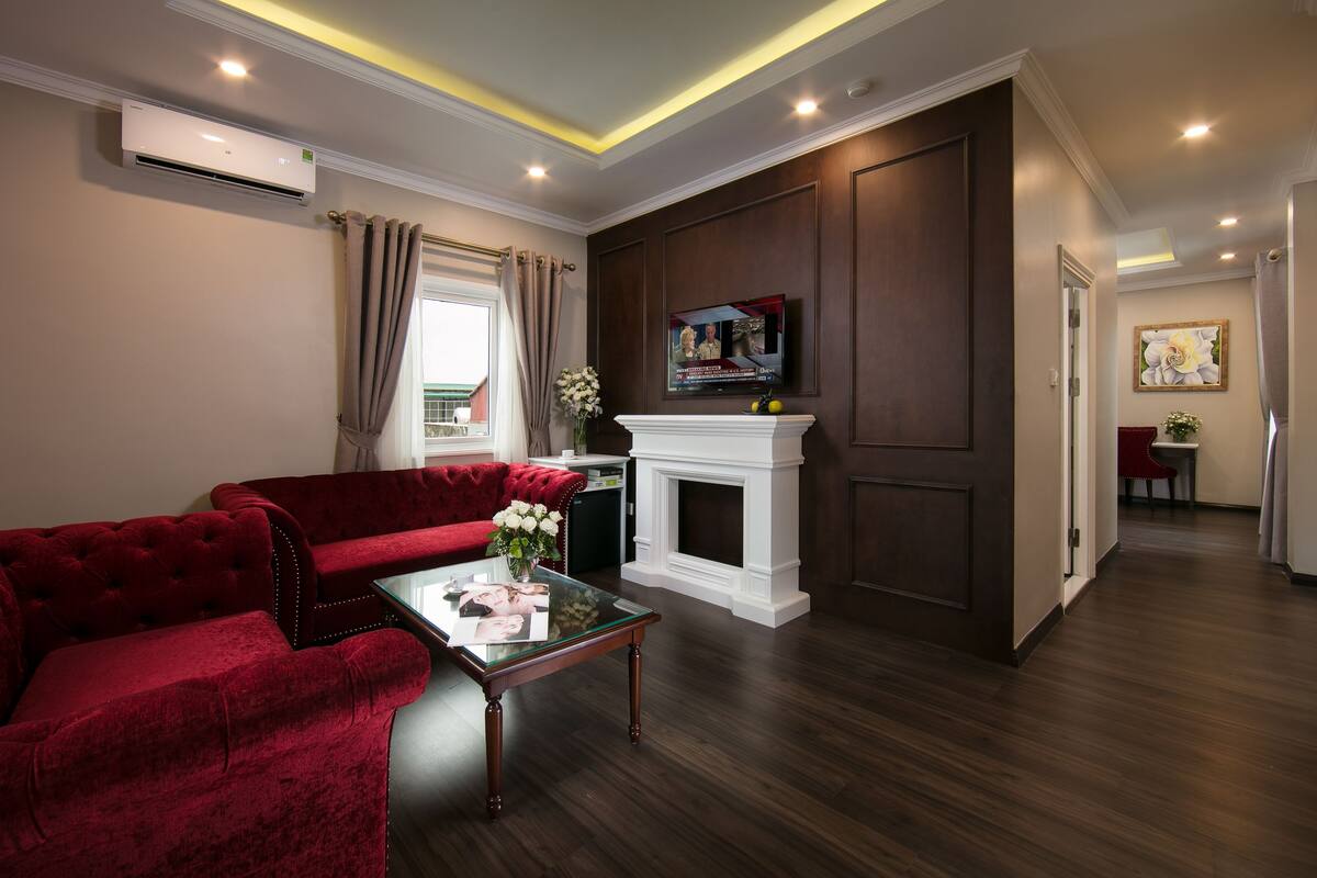 Een woonkamer met een rode bank, een glazen salontafel, een open haard en een aan de muur bevestigde televisie.