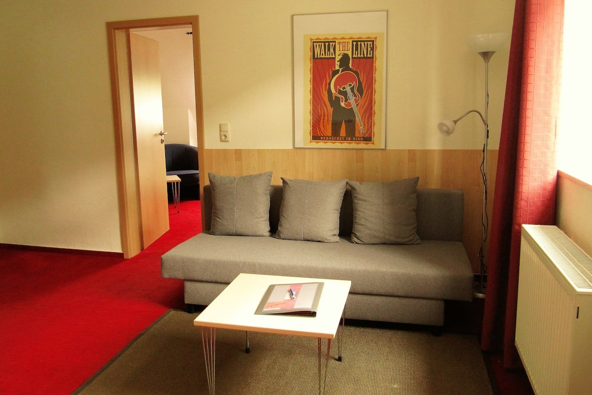 A living room with a grey sofa, a small white table, and a poster on the wall.
