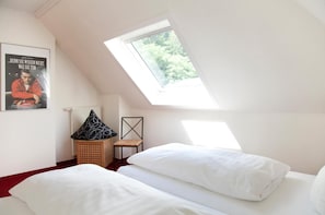 A bedroom with a sloped ceiling, a skylight, a bed with white bedding, a chair, and a poster on the wall. - Hotel Weidenhof (Plettenberg)