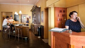 A bar area with stools, a counter, and a woman talking on the phone. - Hotel Weidenhof (Plettenberg)