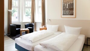 A hotel room with two beds, a desk, a chair, and a window with curtains. - Hotel Weidenhof (Plettenberg)