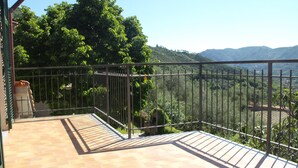 A balcony with a tiled floor, a metal railing, and a view of a mountainous landscape.